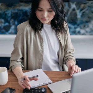 Young woman working on a laptop with notebook and calculator for energy analysis.